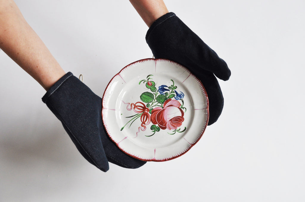 Marineblauwe denim ovenwanten van Ensemble houden een beschilderd bord met bloemen vast